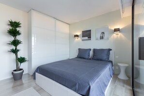 Un dormitorio moderno con una cama grande, dos luces fijadas a la pared y una planta en maceta.