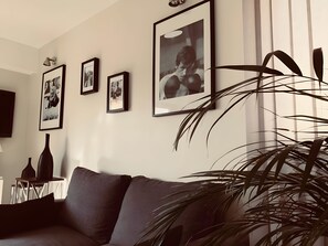 Una sala de estar con un sofá, fotografías enmarcadas en la pared, una lámpara y una planta.