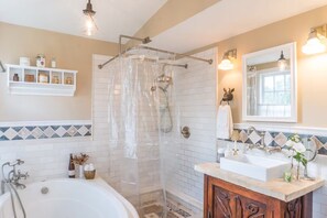 Une salle de bain avec une douche à parois de verre, une baignoire blanche, un meuble-lavabo en bois et un mur recouvert de carreaux.