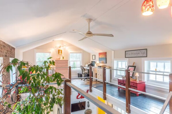 Un loft spacieux avec un plafond haut, un ventilateur de plafond, un escalier et une vue sur l’extérieur.