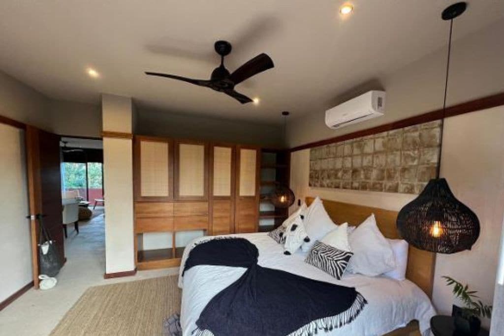 Une chambre à coucher comprenant un lit, un ventilateur de plafond, un appareil de climatisation et un luminaire suspendu.