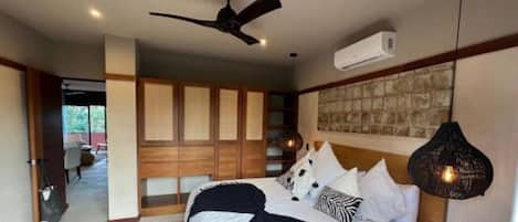 Une chambre à coucher comprenant un lit, un ventilateur de plafond, un appareil de climatisation et un luminaire suspendu.