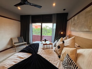 A hotel room with a bed, a chair, a small table, and a view of greenery outside. - Brand New Spacious 4-bedroom condo in lovely Cozumel with Jacuzzi g12 (Cozumel)