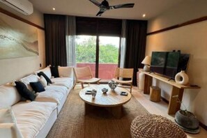 A hotel room with a sofa, a round coffee table, a television, and a window with curtains. - Brand New Spacious 4-bedroom condo in lovely Cozumel with Jacuzzi g12 (Cozumel)