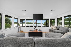 Ein modernes Wohnzimmer mit großen Fenstern, einem Flachbildfernseher und grauen Sofas.