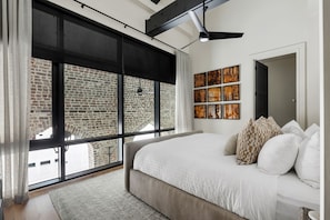 Un dormitorio moderno con una cama grande, vista a un edificio de ladrillo y obras de arte en la pared.