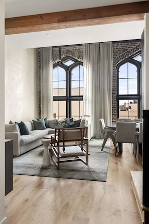 Un salón amplio con un gran ventanal, un sofá, una mesa de comedor y una silla de madera.