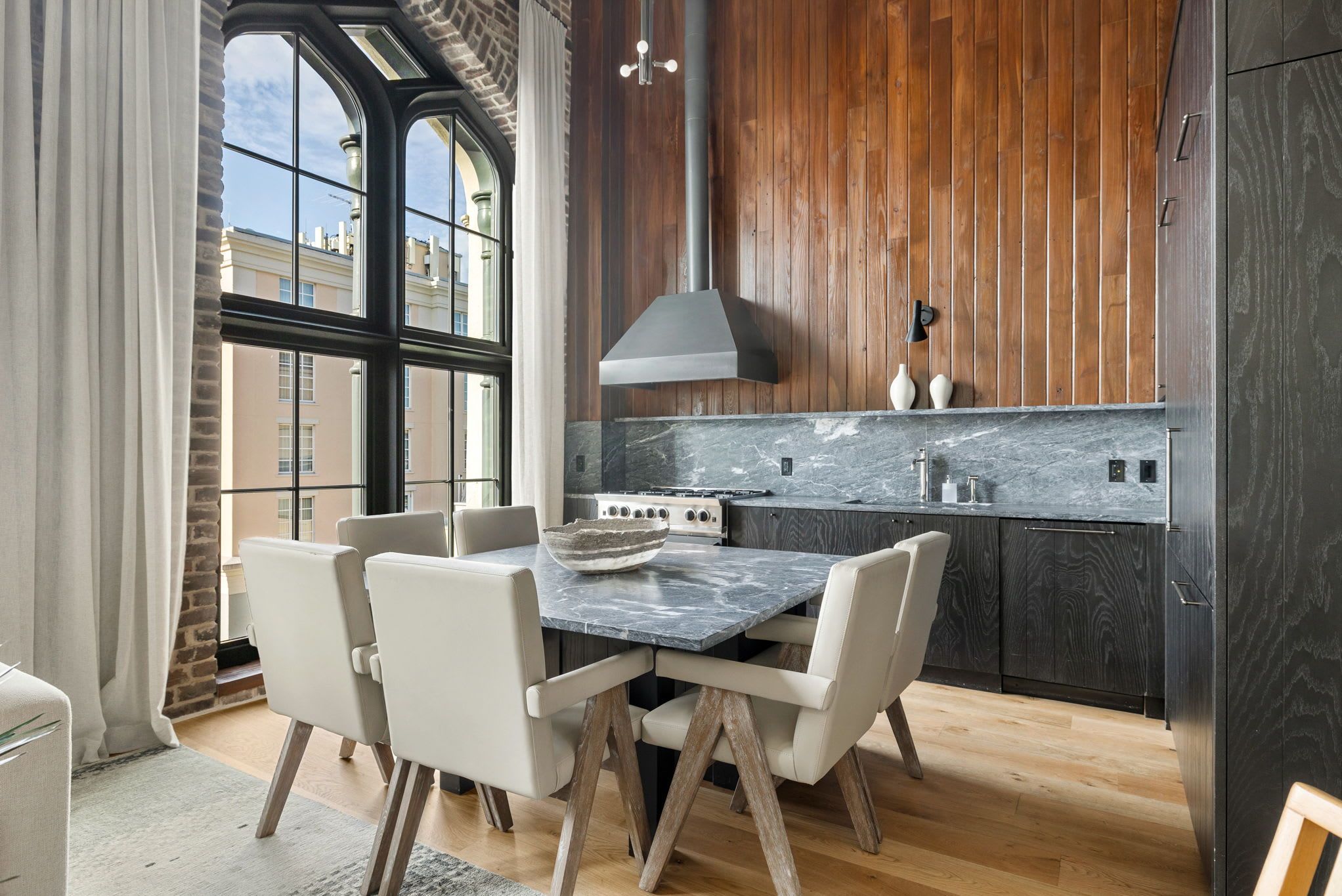 A modern kitchen with a dining table and chairs, wooden cabinets, and a large window.