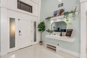 A modern interior with a white door, a potted plant, a mirror, and a welcome sign. - Elite Luxury Pickleball Palace-Heated Pool (Scottsdale)