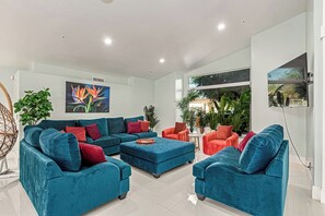 A modern living room with a sectional sofa, armchairs, a coffee table, and a large window with a view of greenery. - Elite Luxury Pickleball Palace-Heated Pool (Scottsdale)