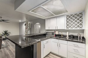 A modern kitchen with white cabinets, a black countertop, and a ceiling vent. - Elite Luxury Pickleball Palace-Heated Pool (Scottsdale)