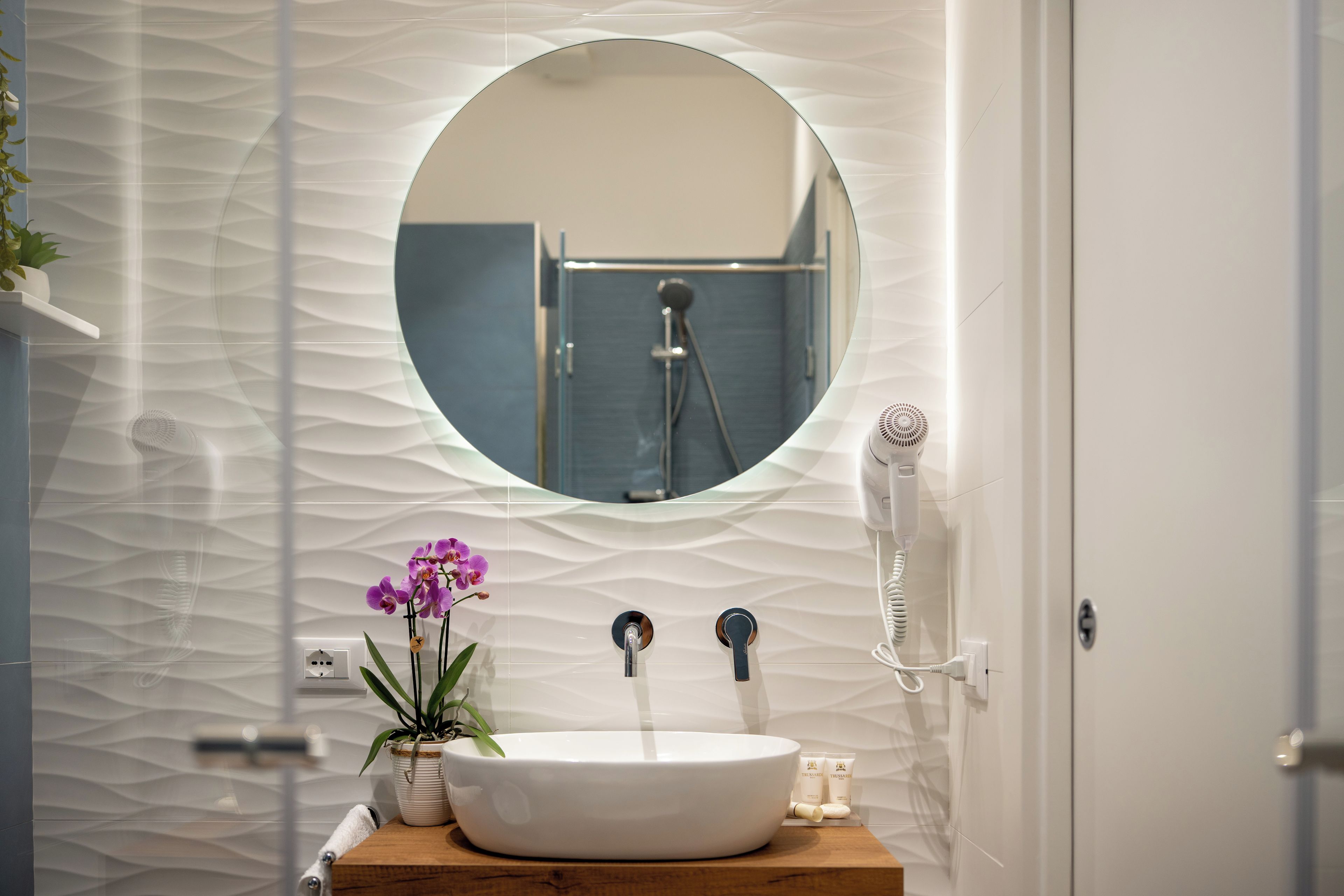Ein Badezimmer mit rundem Spiegel, Waschbecken, Duschbrausehandstück und Föhn.