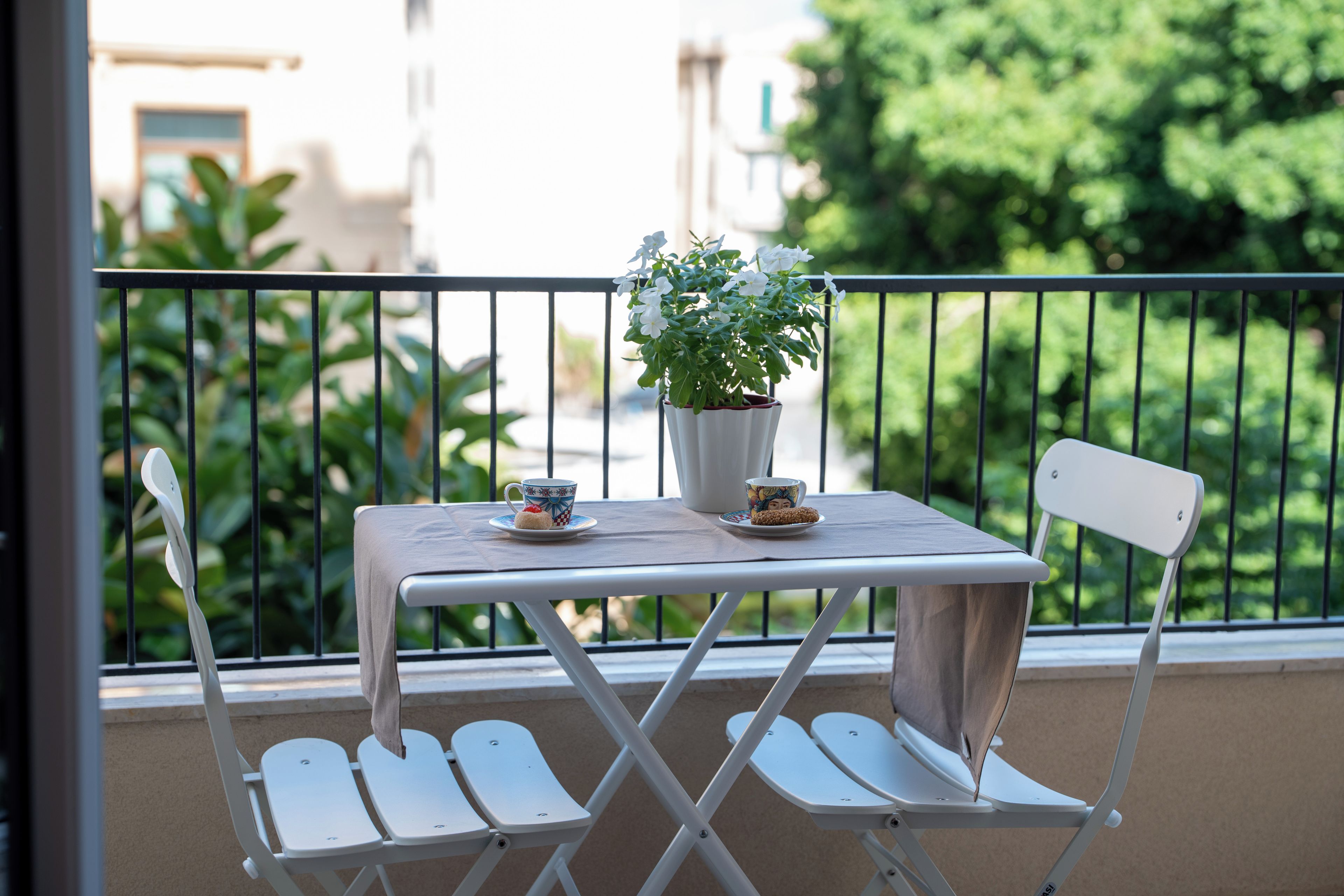 Ein Balkon mit Tisch, Stühlen, einer Topfpflanze und einer Tasse mit Untertasse.