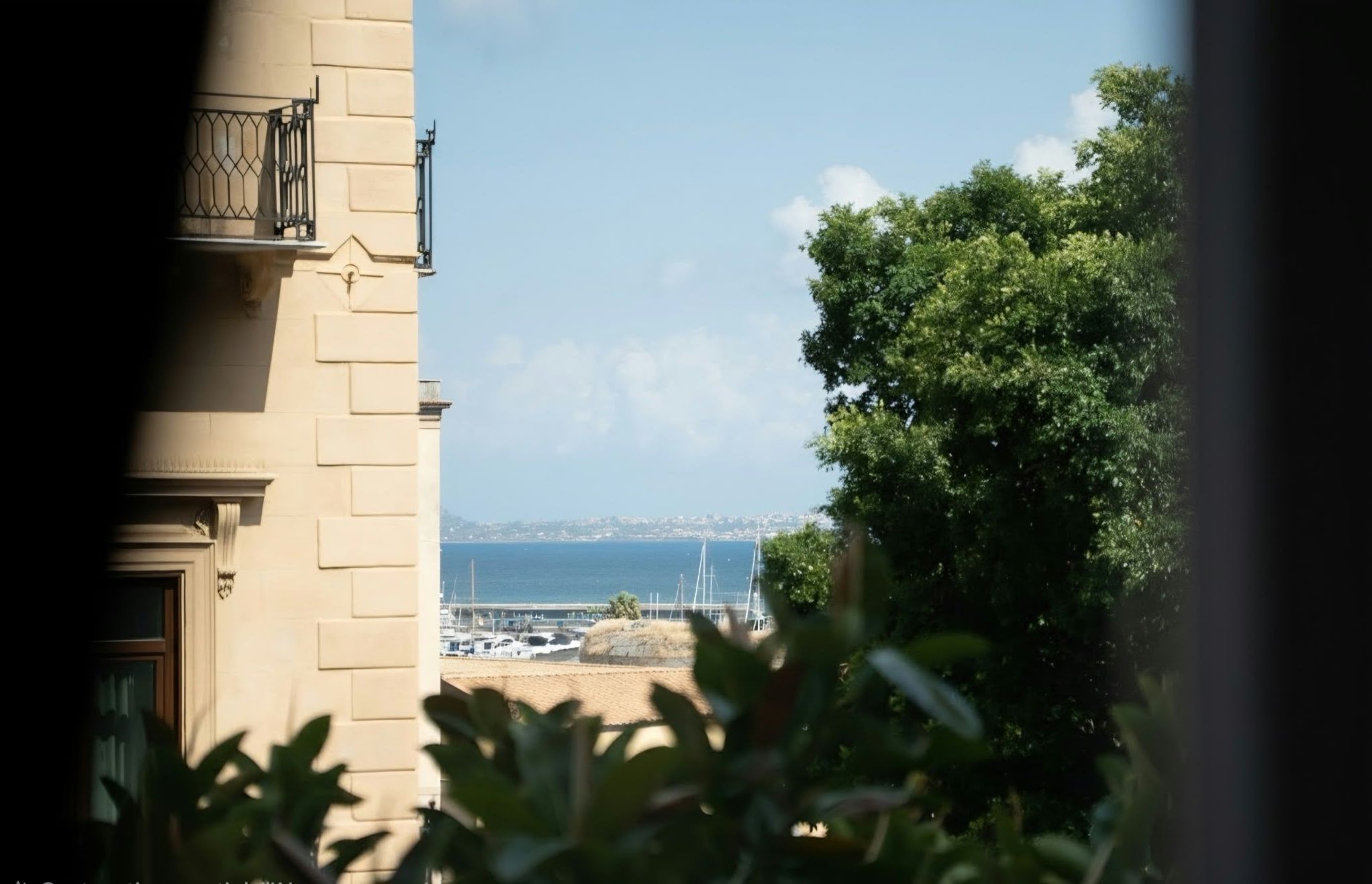A view of a building with a balcony, a clear sky, and a distant view of a body of water with a bridge.