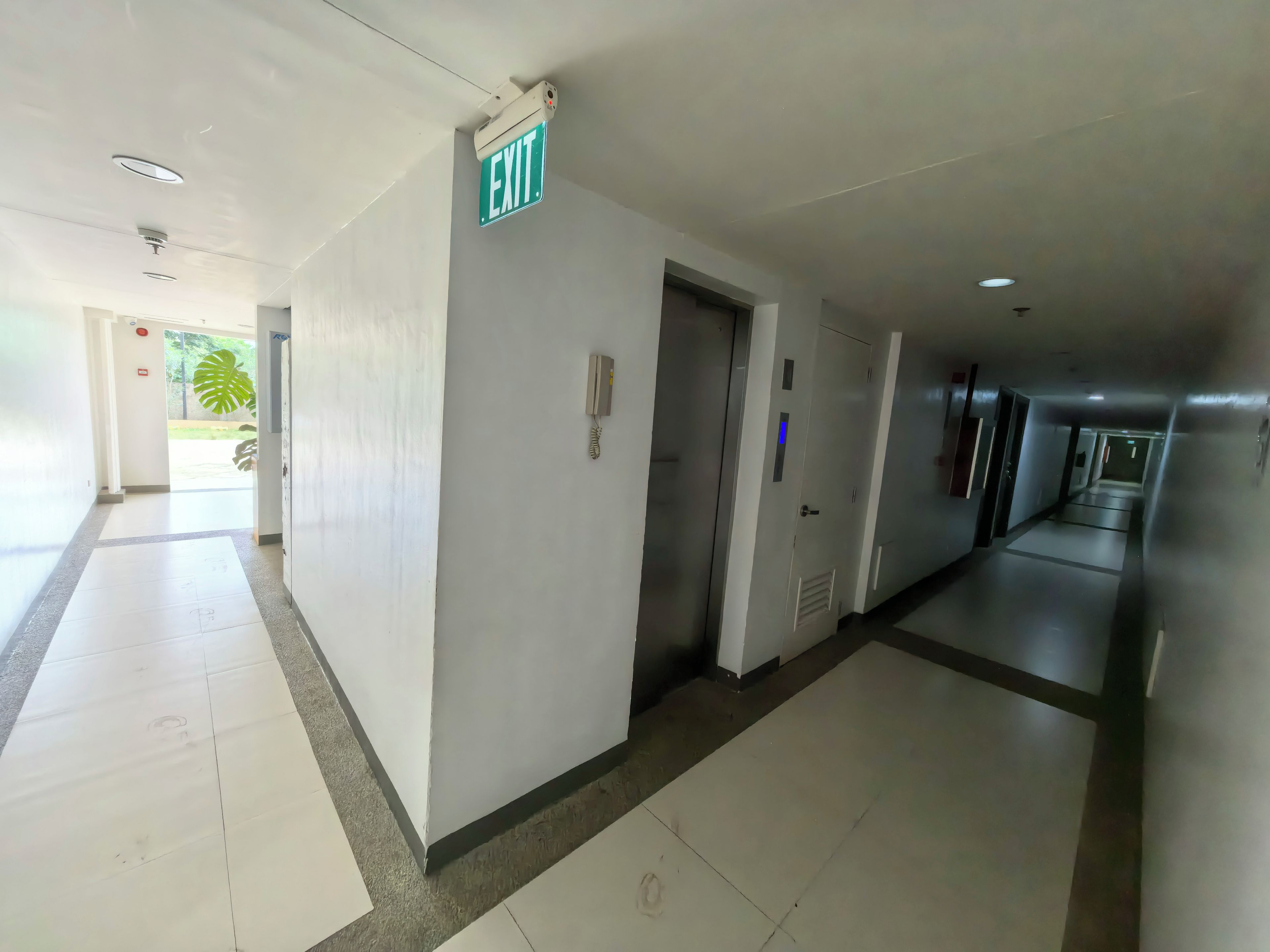 A hotel corridor with an exit sign, a phone, and a door.