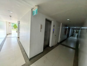 A hotel corridor with an exit sign, a phone, and a door. - Verdant Condo Studio, Pool, Gym, Balcony & Near Airport (PUERTO PRINSESA)