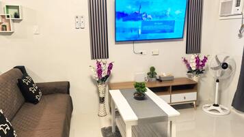 Ein modernes Wohnzimmer mit einem an der Wand befestigten Flachbildfernseher, einem braunen Sofa, einem weißen Couchtisch und zwei Zimmerpflanzen.
