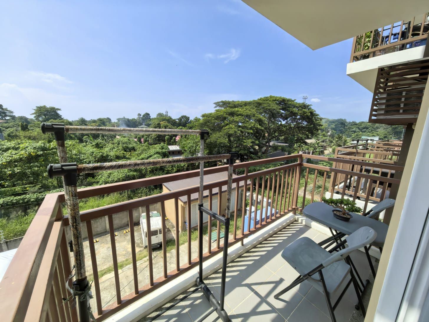 A balcony with a view of a lush green landscape, a table with chairs, and a railing.