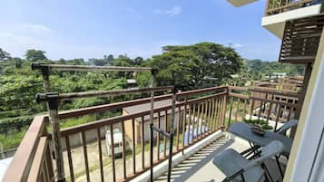 A balcony with a view of a lush green landscape, a table with chairs, and a railing.
