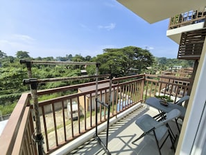 A balcony with a view of a lush green landscape, a table with chairs, and a railing. - Verdant Condo Studio, Pool, Gym, Balcony & Near Airport (PUERTO PRINSESA)