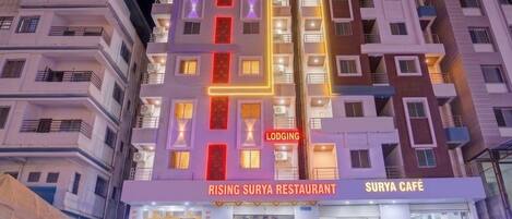 Un edificio de varios pisos con letreros que indican 'AC ROOMS', 'LODGING', 'RESTAURANTE RISING SURYA' y 'CAFÉ SURYA'.