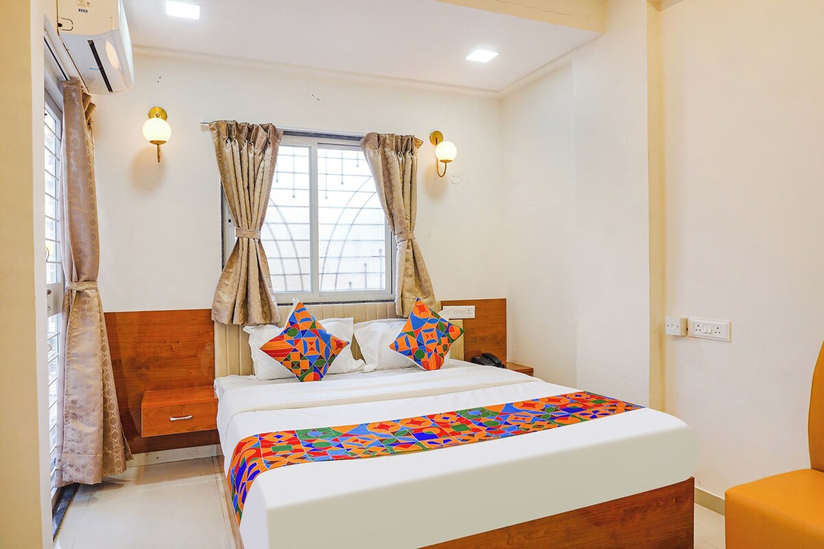 A hotel room with a bed, a bedside table, a lamp, and a window with curtains.