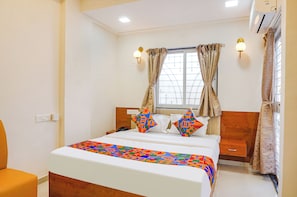 A hotel room with a bed, bedside table, and a window with curtains. - RISING SURYA HOTEL (Pune)