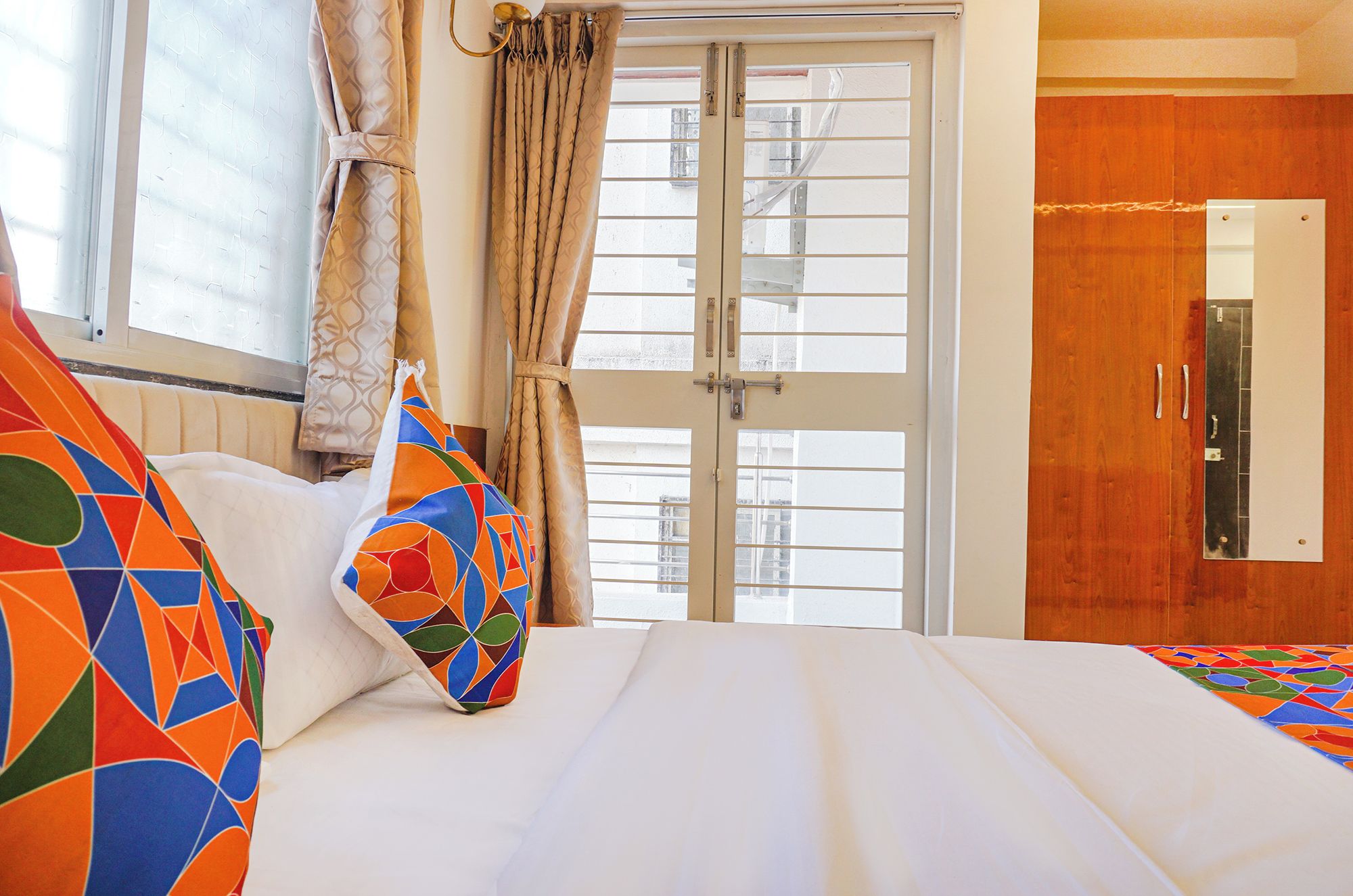 Una habitación de hotel con cama, ventana con cortinas y un armario de madera.