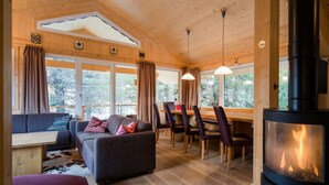 Interior acolhedor de uma cabana, com sofá, mesa de jantar, cadeiras e lareira a lenha.