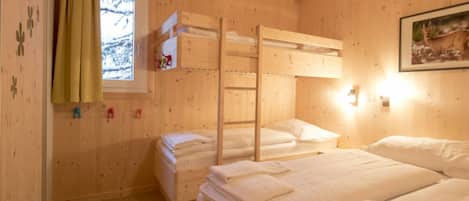 Una habitación de cabaña de madera con literas, una ventana con cortinas y una lámpara fijada a la pared.