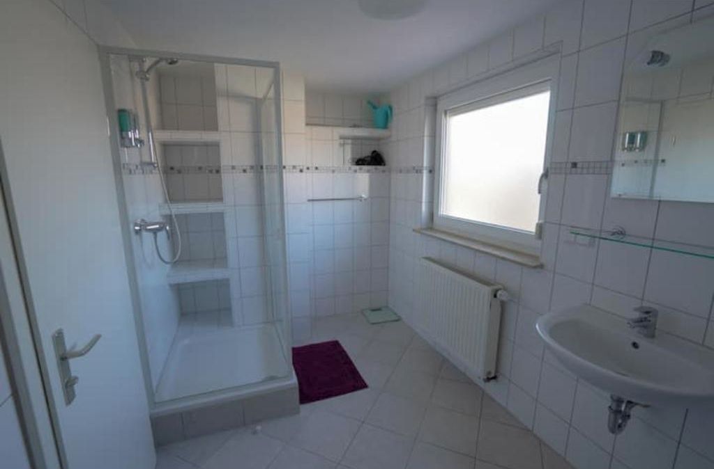 Une salle de bain avec une douche à parois de verre, un lavabo et une fenêtre.