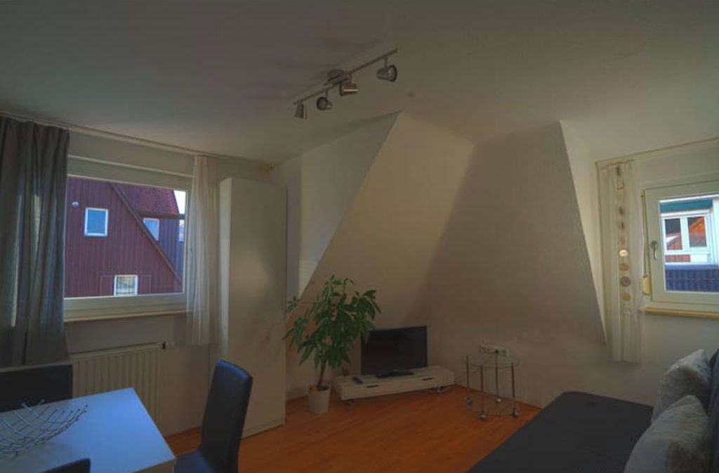 Une pièce avec un plafond en pente, un téléviseur posé sur un meuble, une plante en pot et une fenêtre avec des rideaux.