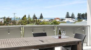 A balcony with a wooden table and chairs, overlooking a coastal area with trees and buildings. - Coastal luxury home with breathtaking ocean and harbour views (Robe)