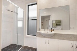 Une salle de bain moderne avec une douche à parois de verre, un grand miroir et un lavabo blanc doté d’un plan de travail.