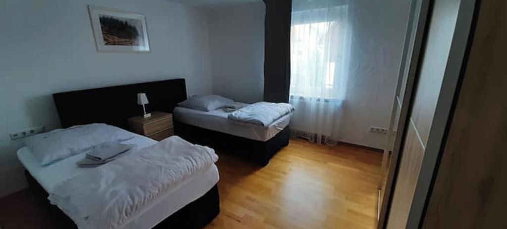 Een kamer met twee bedden, een nachtkastje en een raam met dunne gordijnen.