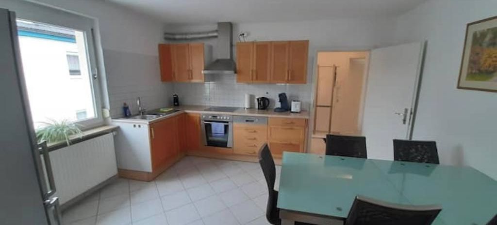 Cozinha compacta com armários de madeira, forno embutido e mesa de jantar com cadeiras.