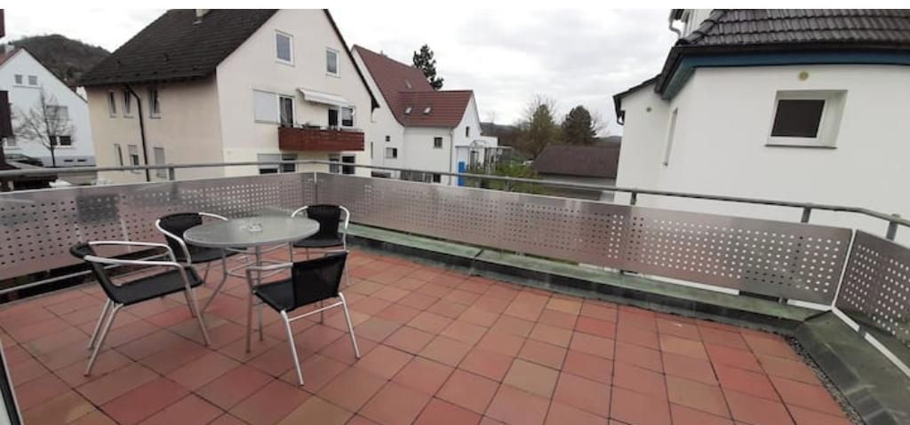Une terrasse sur le toit, avec une table et des chaises, entourée d’une rambarde en métal.