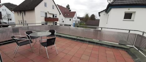 Une terrasse sur le toit, avec une table et des chaises, entourée d’une rambarde en métal.