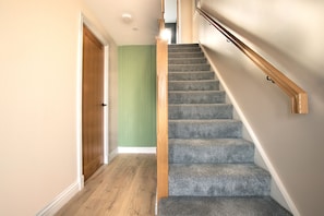 A staircase with carpeted steps and wooden handrails, leading to a room with a green wall and a wooden door. - St Andrews Golf House | Private Sim & Cinema (St Andrews)