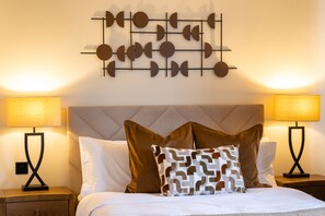 A neatly made bed with white bedding and two decorative pillows, flanked by two bedside lamps on wooden nightstands. - St Andrews Golf House | Private Sim & Cinema (St Andrews)