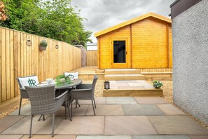 A patio area with a wooden fence, a small wooden building with a door, and a table with chairs. - St Andrews Golf House | Private Sim & Cinema (St Andrews)