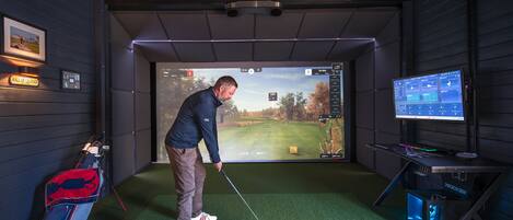 A golf simulation room with a large screen, a golf cart, and a golf bag.