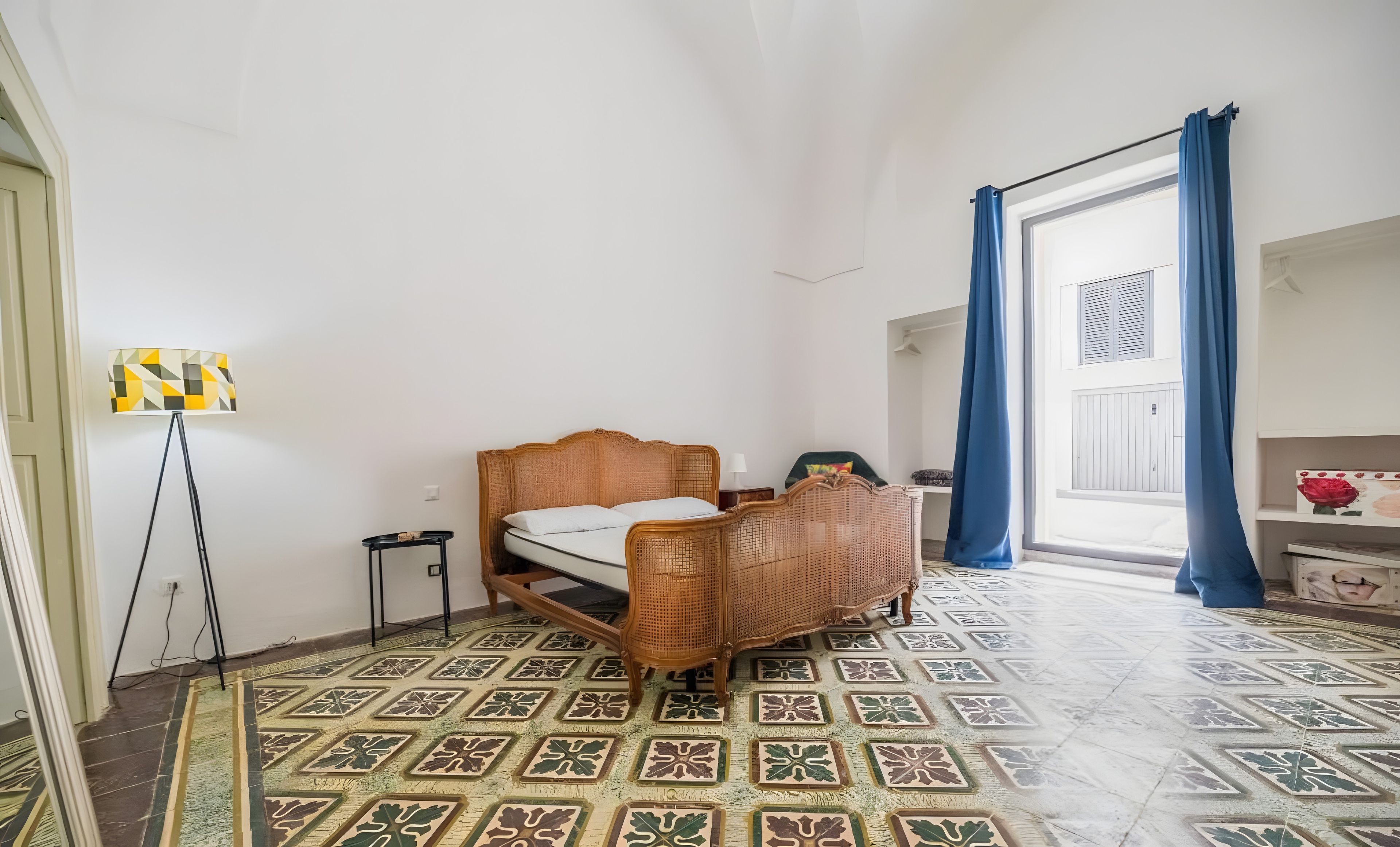 Ein Zimmer mit einem Bett, einer Stehlampe und einem gemusterten Boden.