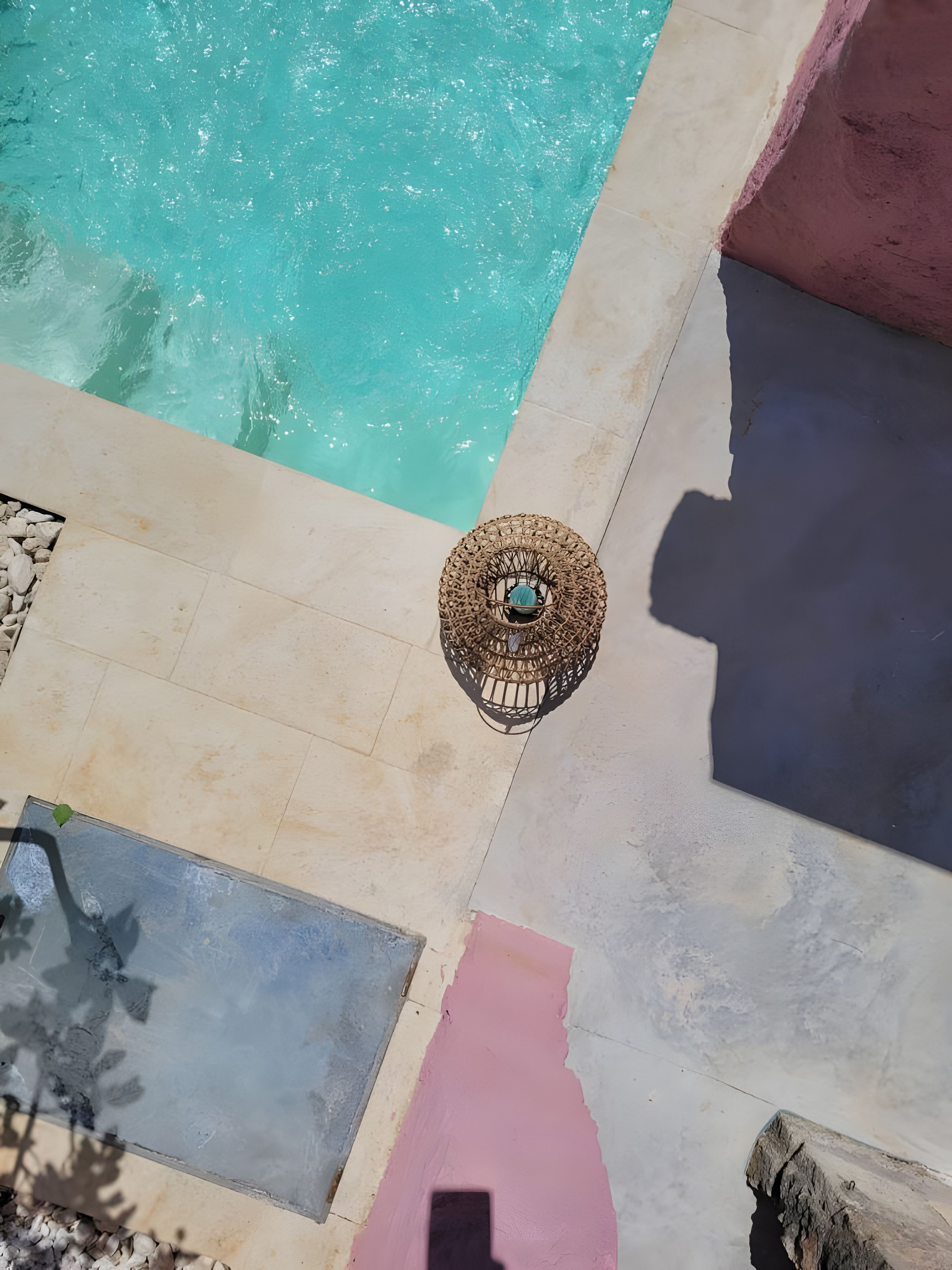 Ein Pool mit klarem Wasser, ein Korbsonnenschirm und eine geflieste Liegefläche.