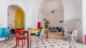 Un área de comedor con una mesa de madera, sillas coloridas y un sofá azul en una habitación con arcos blancos y una pared amarilla.