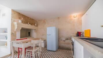 A compact kitchen with a checkered floor, a white table with red chairs, a blue refrigerator, and a small sink.