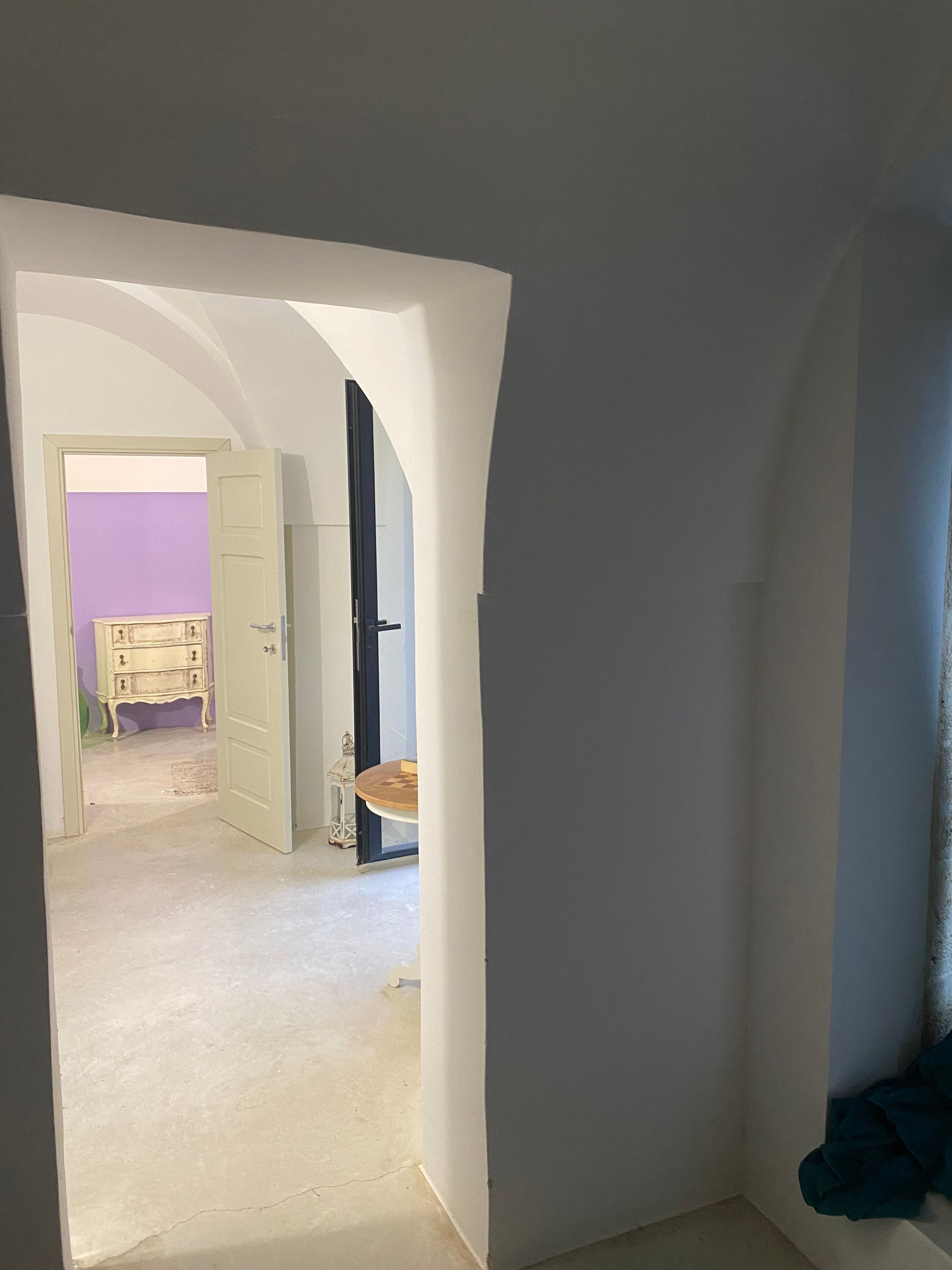 Ein Flur mit geöffneter Tür, die zu einem Raum mit violettem Wand und weißem Schminktisch führt.