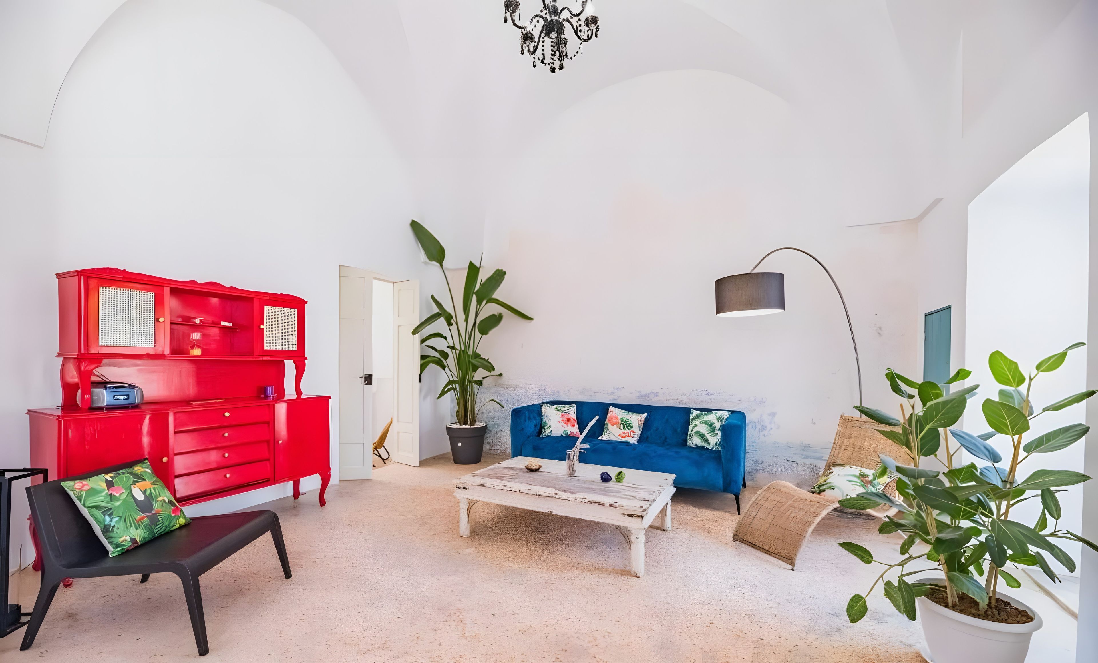 A room with a red dresser, a blue sofa, a white coffee table, and a potted plant.