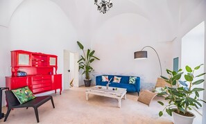 Et værelse med en rød kommode, en blå sofa, et hvidt sofabord og en potteplante.