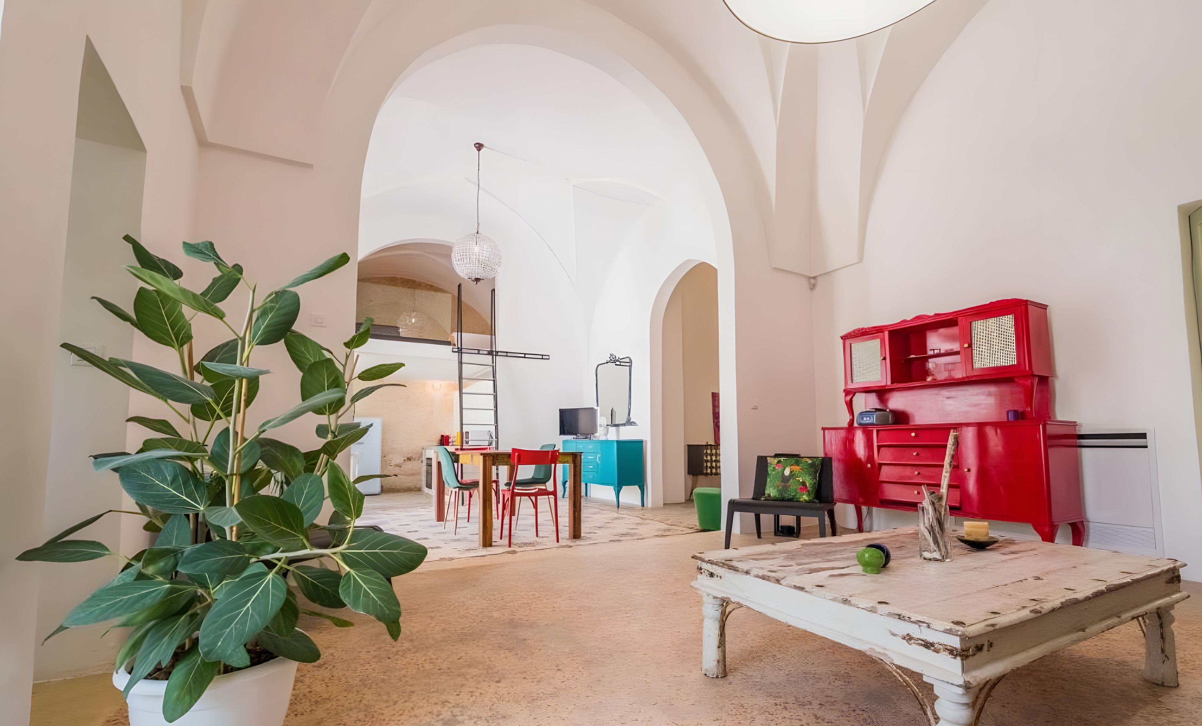 Une pièce avec une grande plante, une table sur laquelle se trouve un objet vert et un meuble rouge.